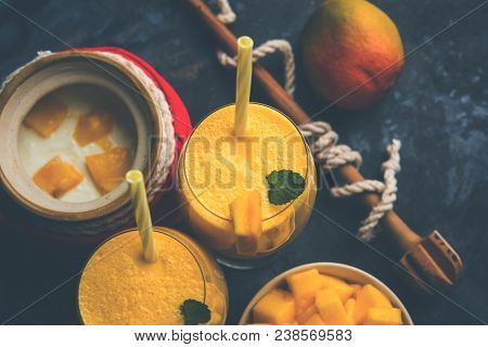 Mango Lassi Or Smoothie In Big Glass Or Small Bottles With Curd, Cut Fruit Pieces And Blender. Moody