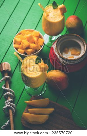 Mango Lassi Or Smoothie In Big Glass Or Small Bottles With Curd, Cut Fruit Pieces And Blender. Moody