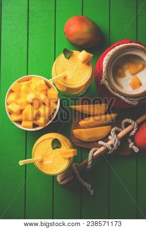 Mango Lassi Or Smoothie In Big Glass Or Small Bottles With Curd, Cut Fruit Pieces And Blender. Moody