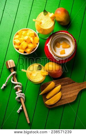 Mango Lassi Or Smoothie In Big Glass Or Small Bottles With Curd, Cut Fruit Pieces And Blender. Moody