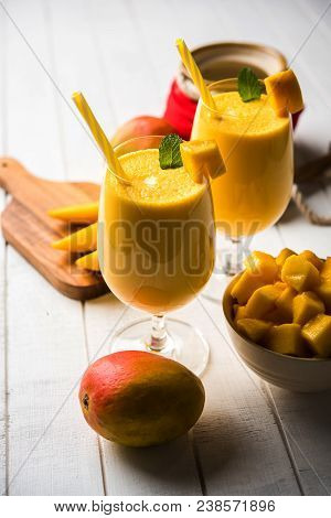 Mango Lassi Or Smoothie In Big Glass Or Small Bottles With Curd, Cut Fruit Pieces And Blender. Moody