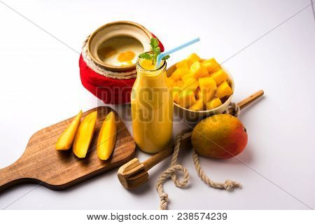 Mango Lassi Or Smoothie In Big Glass Or Small Bottles With Curd, Cut Fruit Pieces And Blender. Moody