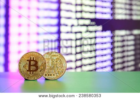 Two Gold Bitcoins Lie On The Green Surface On The Background Of The Display, Which Shows The Process