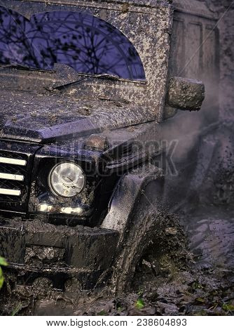 Fragment Of Dirty Offroad Car, Close Up. Suv Covered With Mud Stuck In Puddle. Black Crossover Drivi