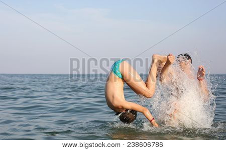 Boy Takes A Dive Upside Down In The Sea, Spraying Water Helped By His Father
