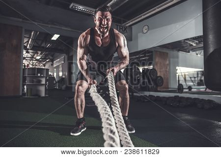 Muscular Powerful Aggressive Man Working Out With Rope In Functional Training Fitness Gym