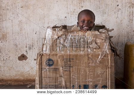 Nhacra, Republic Of Guinea-bissau - January 28, 2018: Portrait Of A Young Boy Playing In A Card Box 
