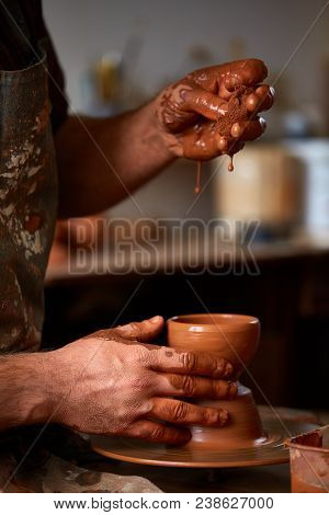 Close-up Hands Of A Male Potter In Plaid Shirt And Dirty Apron Who Molds A Vase From Clay, Selective