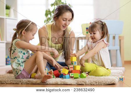 Family Activities In The Children Room. Mother And Her Kids Daughters Sitting On The Foor And Playin