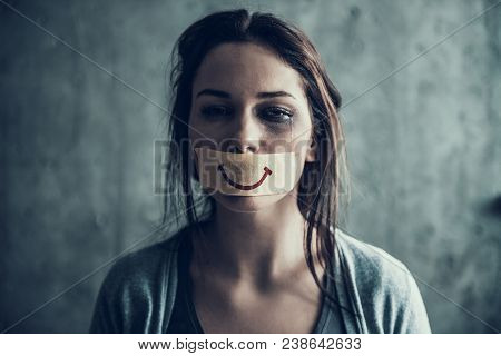 Oppressed Beaten Woman Cries. Gag Of Insulating Tape With Picture Of Smile. Victim Of Tyranny.