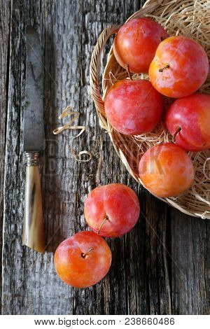 Red Plums In Wicker Basket On Old Wooden Background. Top View
