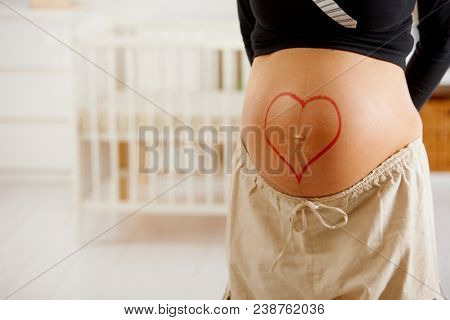 Close-up of pregnant belly with drawn heart shape.
