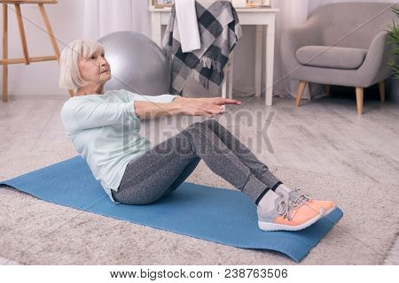 I Love Fitness. Charming Elderly Woman Sitting On The Yoga Mat And Doing Sit-ups, Trying To Work Out