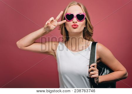 Nice Girl With Glasses And Black Bag Is Loooking Straight. She Is Showing The Piece Symbol And Putti