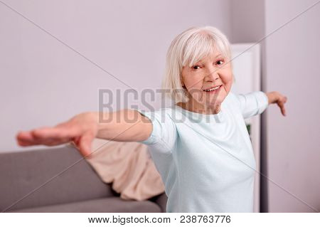 Effective Warm-up. Charming Elderly Woman Doing A Warm-up Before Working Out And Spreading Her Arms 