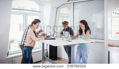 Busy co-workers using mobile technology connected to WI-FI network while sharing a desk in a modern work hub for freelancers and nomad entrepreneurs