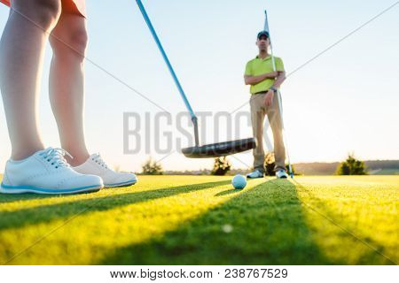Golf ball in selective focus under the putter club of a female player exercising on the putting green during class with an experienced teacher