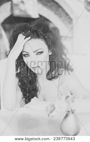 Pretty Sexy Young Brunette Woman With Curly Hair And Bright Makeup Sitting In Cafe At Table With Vas