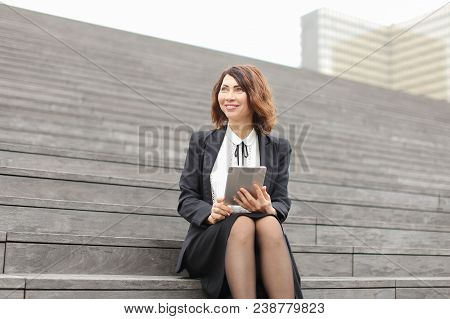 Female Caucasian Manager Sitting On Stairs With Tablet. Concept Of Working In Open Ait And Modern Te