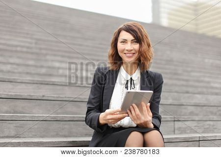Female Administrator Sitting On Stairs With Tablet. Concept Of Working In Open Ait And Modern Techno