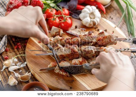 Rustic. Hands Cut A Juicy Pork Meat With A Knife. Appetizing Shish Kebabs And Fresh Vegetables On A