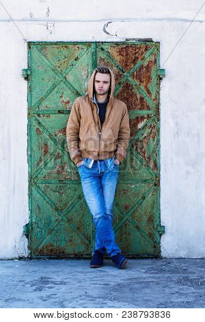 A Young Handsome Man In A Hood On The Background Of A Rusty Door
