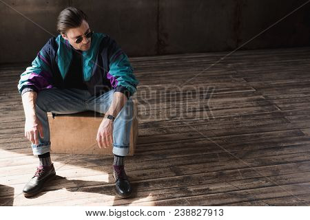 Stylish Young Man In Vintage Windcheater Sitting On Wooden Box In Loft Room