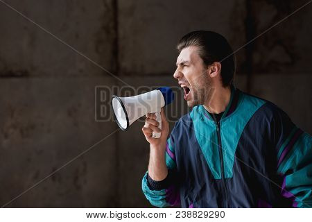 Side View Of Angry Young Man In Vintage Windcheater Shouting With Loudspeaker