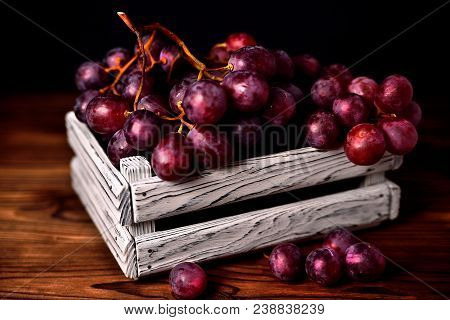 Branch Of A Dark Grapes In A White Box On A Wooden Background