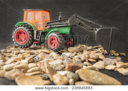 Close Up Of Children Colored Plastic Miniature Of Construction Machine Vehicle Over Grawel Stones. I