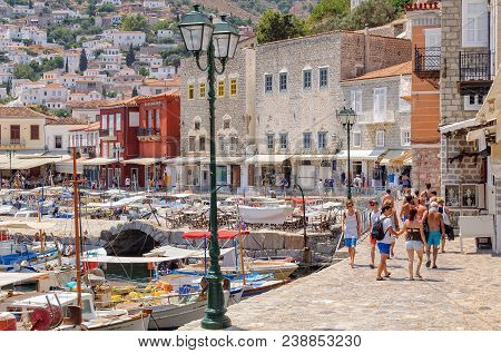 Tourists Walk Around The Small Boat Filled Harbor Ringed With Cafes, Restaurants And Shops - Hydra, 
