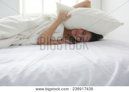 Young caucasian woman covering her head and ears with pillows
