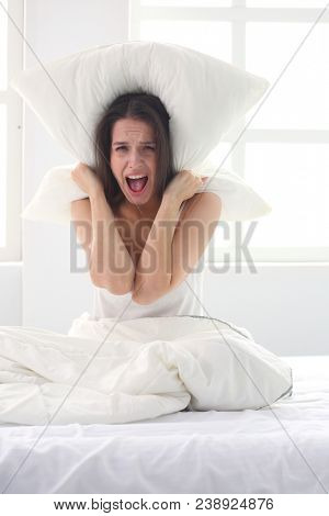 Young caucasian woman covering her head and ears with pillows