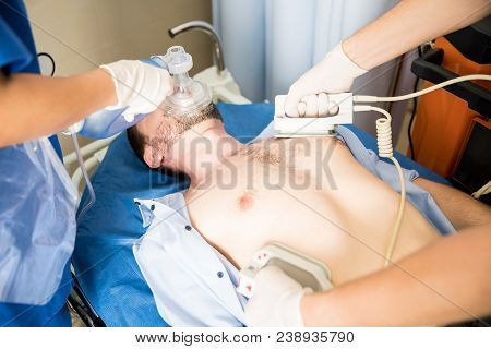 Close Up Of Emergency Medical Team Resuscitating Patient With A Defibrillator And Ambu Bag In Hospit