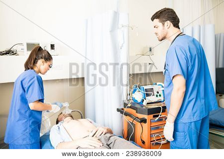Male And Female Doctors Working On An Unconscious Patient In Emergency Room