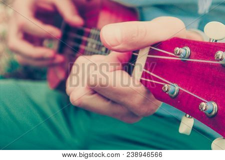 Photo Depicts Musical Instrument Ukulele Guitar In The Hands Of Player. Musician Fingers Are Playing