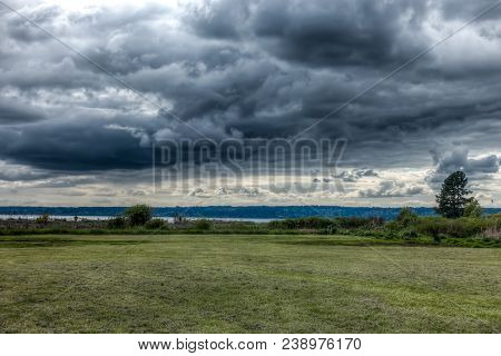 Dark Storm Clouds Hover Over A Green Meadow In Normany Park, Washington.