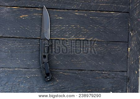 Black Knife With A Black Blade. Dark Wooden Background.
