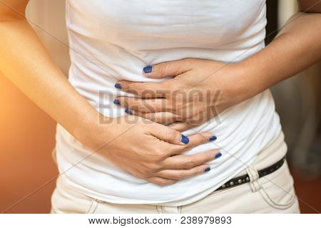 Young Woman Suffering From Abdominal Pain While Sitting On Bed At Home