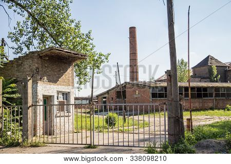 Entrance To An Abandoned Factory And Warehouse With Its Distinctive Brick Chimnet In Eastern Europe,