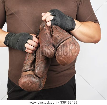 Adult Man In Brown Sport Uniform Holds A Pair Of Brown Vintage Casual Boxing Gloves, White Backgroun