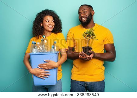 Happy Couple Hold A Plastic Container With Bottles And A Small Tree Over A Light Blue Color. Concept
