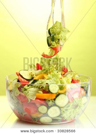 Frischer Gemüsesalat in transparente Schale mit Löffel und Gabel auf grünem Hintergrund