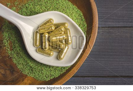 Top View Of Kratom Powder In Ceramic Spoon And Kratom Capsules On Wooden Table