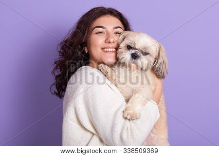 Portrait Of Positive Magnetic Young Girl Holding Maltese In Both Hands, Pressing Its Close To Face, 