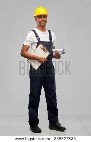 profession, construction and building - happy smiling indian builder in helmet with blueprint and clipboard over grey background