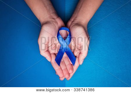 Blue Ribbon In Support Of Trafficking And Sexual Slavery. Blue Ribbon On Female Hands On A Blue Back