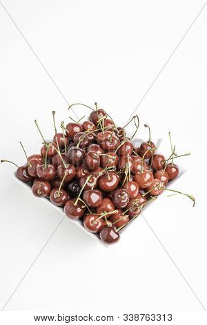 A Bunch Of Fresh Red Cherries Arranged And Fitted In A Square Porcelain Bowl Set On Plain White Back