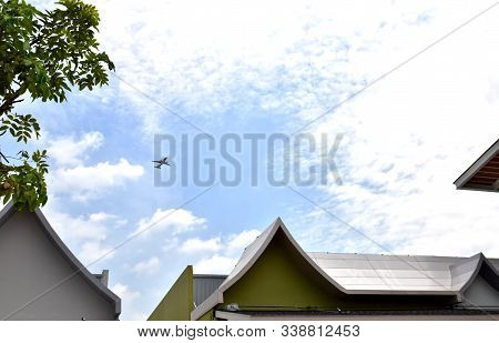 Airplane Fly Above Tree And House In The Sunny Day With Blue Sky And Scattered Clouds.