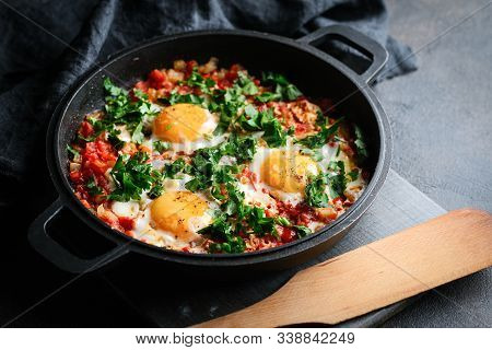 Traditional  Shakshuka With Eggs, Tomato, And Parsley In A Iron Pan On A Dark Background